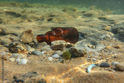 Underwater photo, discarded small beer bottle on sea floor. Ocean littering concept.
