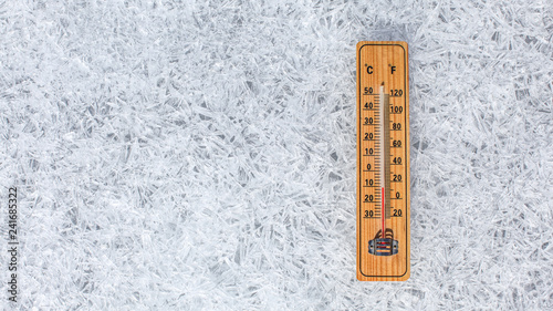 Wooden thermometer showing low temperature laying on flat ice ground made of crystals. Winter weather concept.