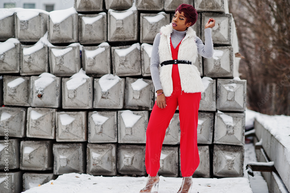 African american woman in red pants and white fur coat jacket posed at winter day against snowy stone background. African american woman in red pants and white fur coat jacket posed at winter day against snowy stone background.