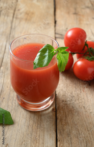 fresh tomato juice in a drinking glass with basil garnish on a rustic wooden table, healthy smoothie drink with copy space, vertical