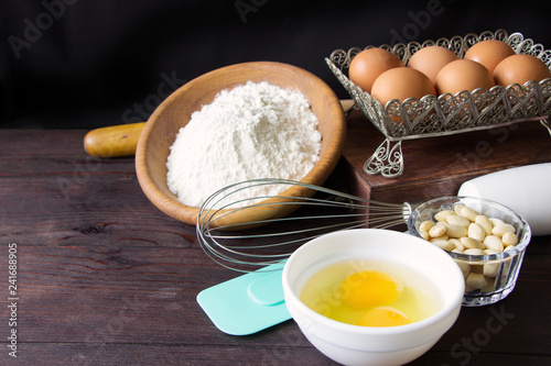 Items and ingredients for baking on a wooden background. Eggs, flour , nuts, rolling pin, wisk and paddle on brown wooden table photo