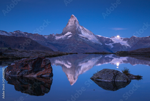 The famous Matterhorn and the moon reflected in the Stellisee before dawn. Zermatt, Switzerland.
