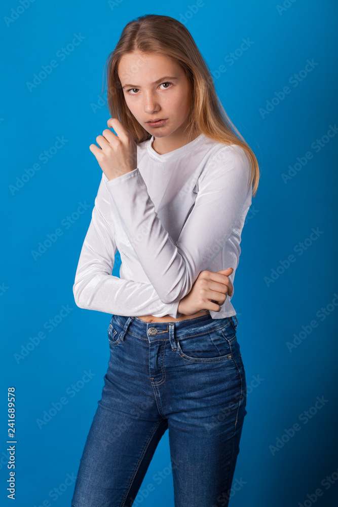 Beautiful smiling teen girl in jeans and a white blouse on blue background. Beautiful smiling teen girl in jeans and a white blouse on blue background.