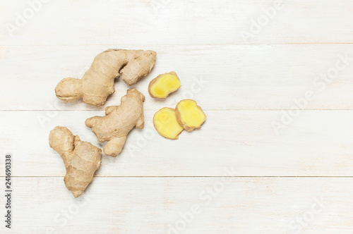 Whole and sliced fresh ginger roots on white wooden background top view copy space. Minimalistic style, seasoning, spice, ingredient for tea. Concept healthy food, medicine, improving immunity