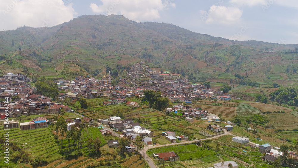 asian town with mosque in mountains among agricultural land, rice terraces. mountains with farmlands, rice fields, village, fields with crops, trees. Aerial view farm lands on mountainside. tropical