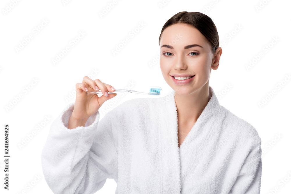 smiling woman in white bathrobe holding toothbrush and looking at camera isolated on white