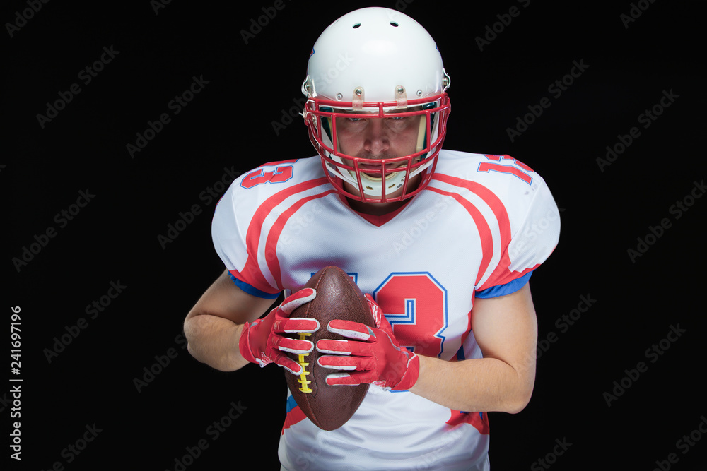 American football player wearing helmet posing with ball on black background American football player wearing helmet posing with ball on black background