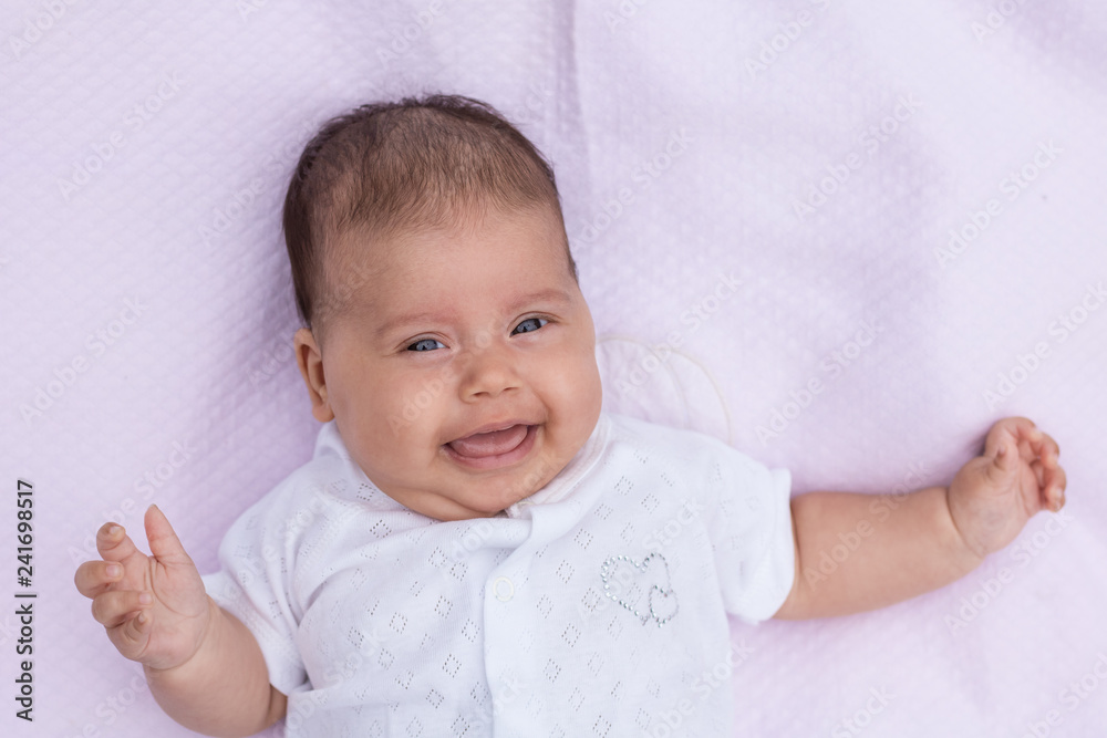 The baby lies on a pink background with a raised hand and crossed fingers, shows a bright emotion. The baby lies on a pink background with a raised hand and crossed fingers, shows a bright emotion.