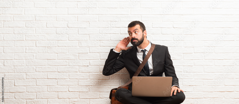 Businessman with his laptop sitting on the floor listening to something by putting hand on the ear Businessman with his laptop sitting on the floor listening to something by putting hand on the ear