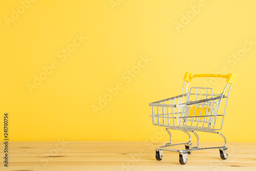 Shopping cart on wooden table with yellow background
