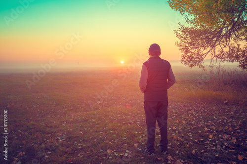 A man stands in the field early in the morning and looks at the sunrise