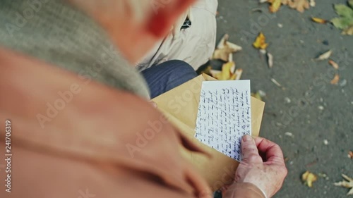 An over the shoulder view of an elderly person opening a handwritten letter in a park with autumn leaves photo