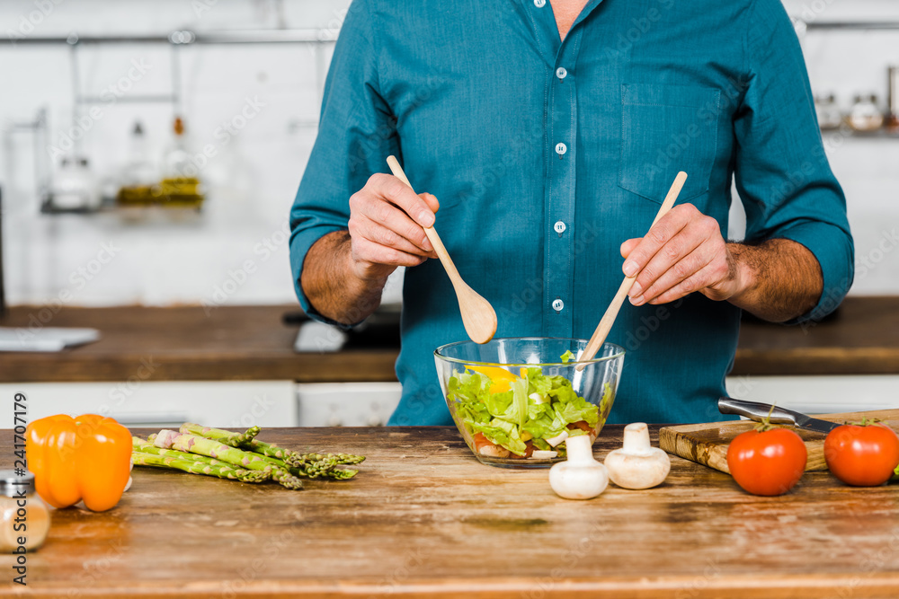 cropped image of mature man mixing salad in bowl in kitchen cropped image of mature man mixing salad in bowl in kitchen