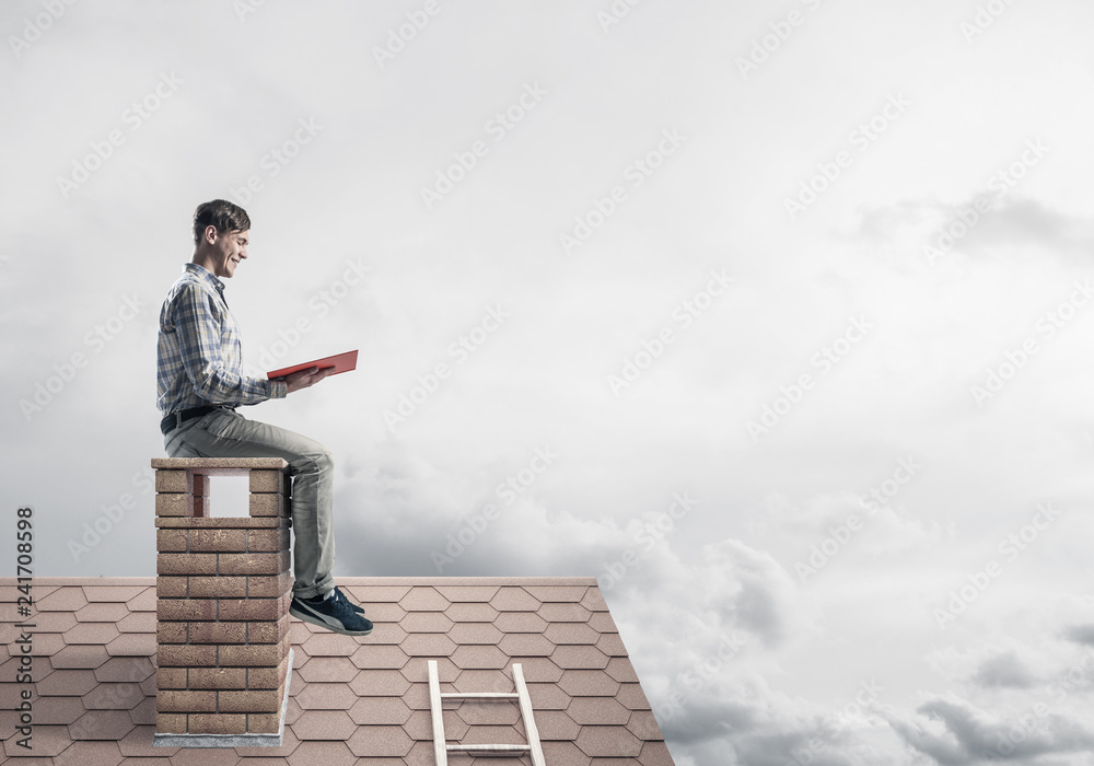 Handsome man on brick roof against cloud scape reading book Handsome man on brick roof against cloud scape reading book