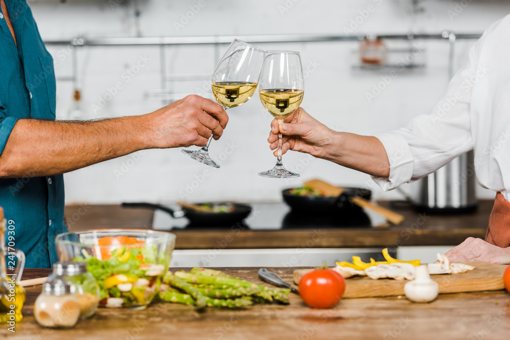 cropped image of wife and husband clinking with glasses of wine in kitchen