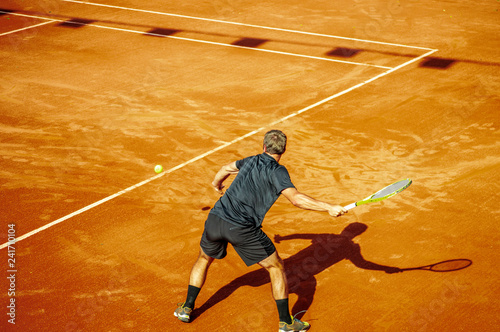 professional male tennis player hitting a forehand in a clay court