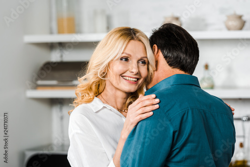 happy mature wife and husband cuddling in kitchen