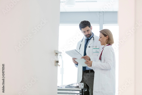 Colleagues discussing over medical records at desk seen through open door in hospital