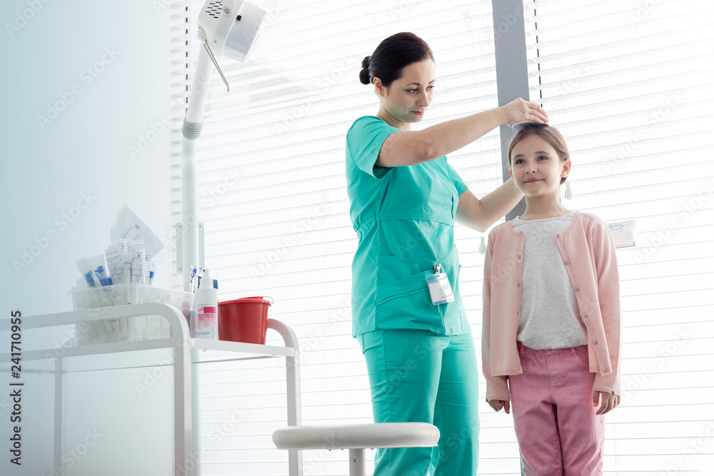 Nurse measuring height of girl against window at examination room - obrazy, fototapety, plakaty 