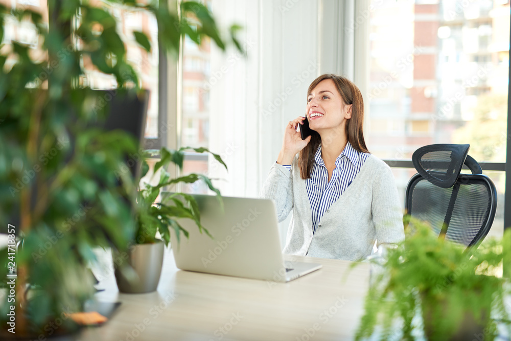 Young woman talking over smartphone while sitting in office
Young woman talking over smartphone while sitting in office
