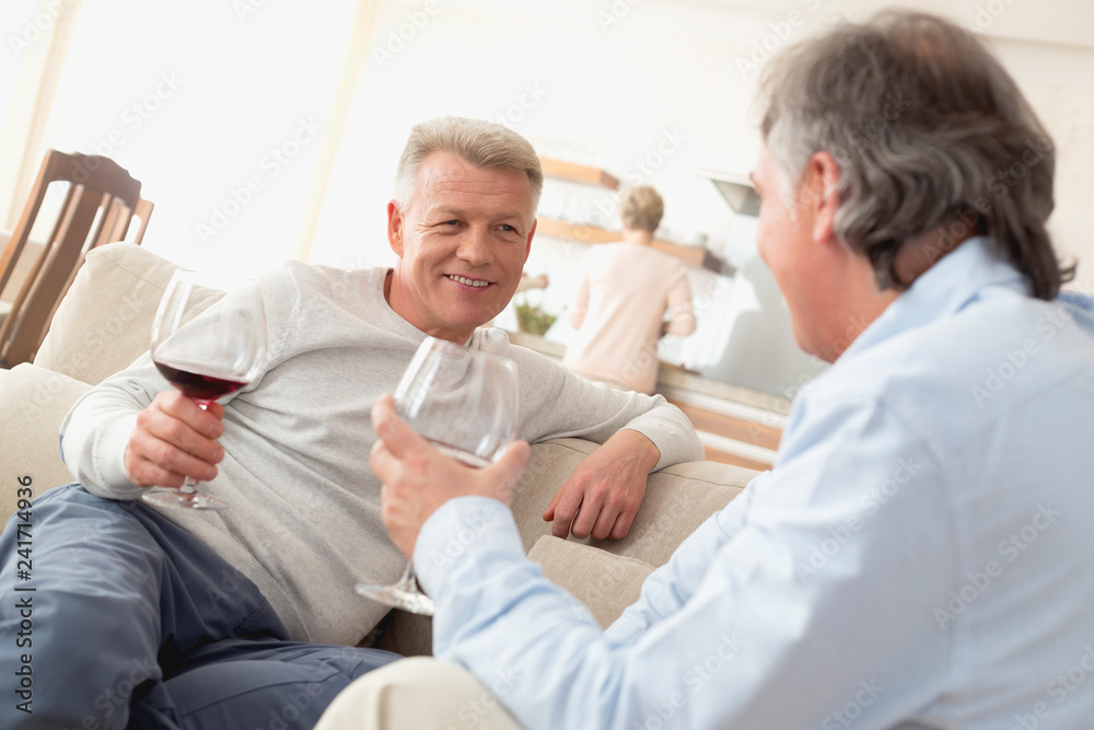 Fototapeta premium Smiling mature men talking while sitting in living room at home