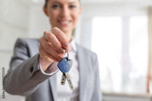 Portrait of smiling young saleswoman giving house keys in apartment