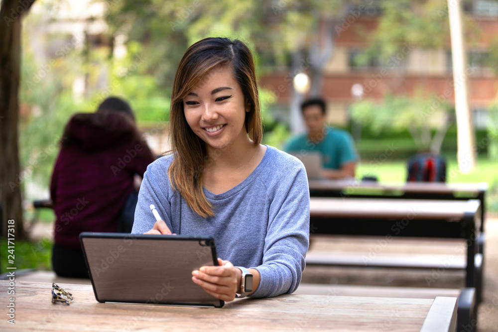 Students working remotely on assignments, outdoor school campus, with laptops and tablets Students working remotely on assignments, outdoor school campus, with laptops and tablets