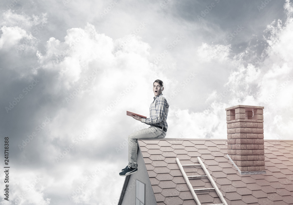 Handsome man on brick roof against cloud scape reading book Handsome man on brick roof against cloud scape reading book