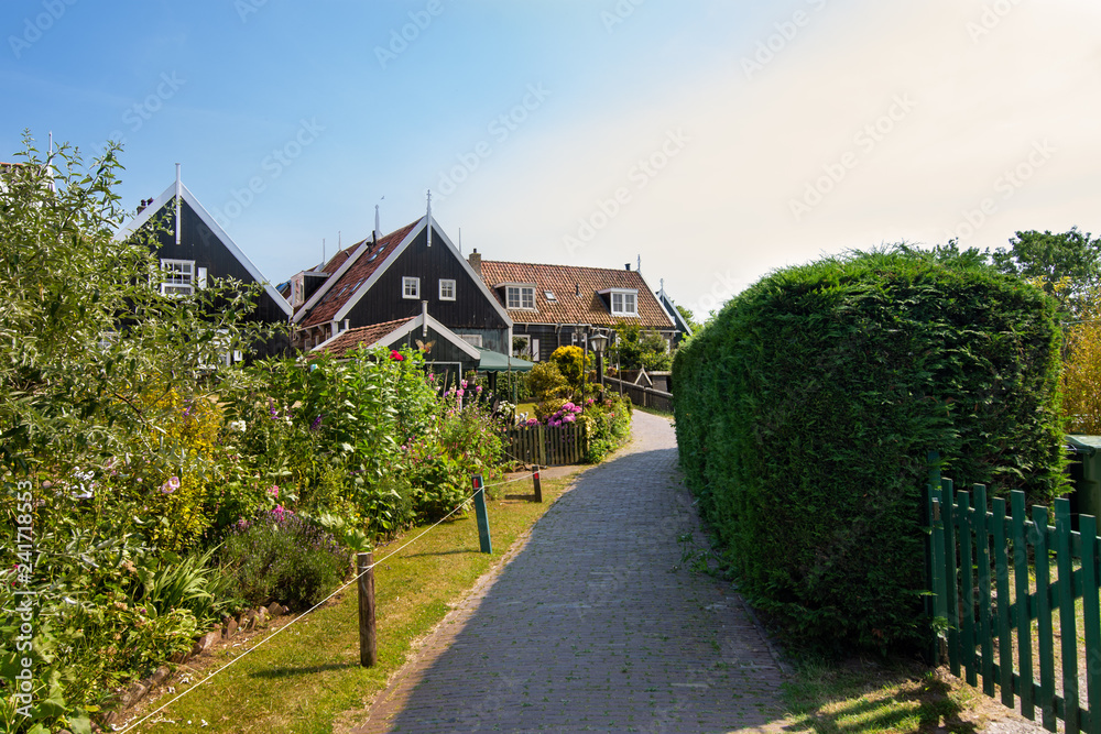 narrow street of Marken houses, Netherlands, Europe. Green gardens and blue sky on a sunny day at sunset