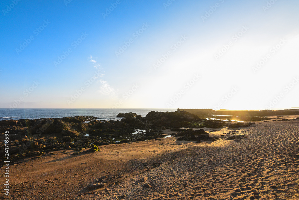Rocky and sandy beach at sunset, with a blue sky, in Porto, Portugal