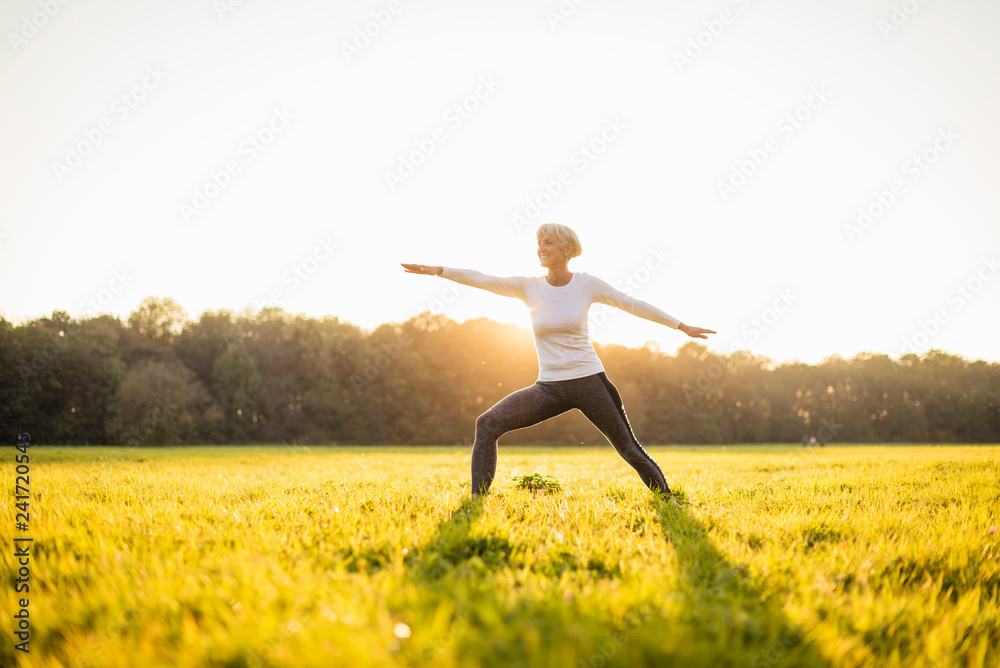 Senior woman doing yoga on rural meadow at sunset Senior woman doing yoga on rural meadow at sunset
