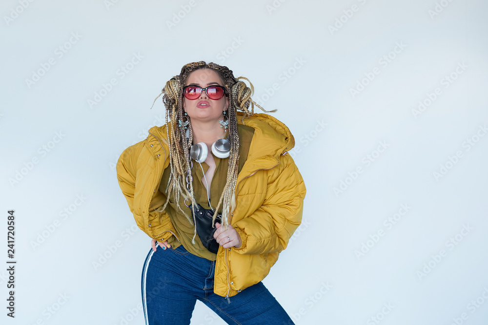 young blonde girl in sunglasses with african pigtails listens to music in headphones and dances against a white background. young blonde girl in sunglasses with african pigtails listens to music in headphones and dances against a white background.