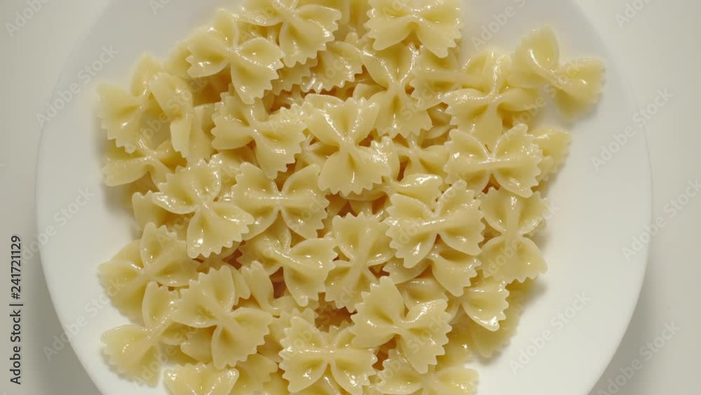 SLOW MOTION: Farfalle pasta falling into a white plate - Top View SLOW MOTION: Farfalle pasta falling into a white plate - Top View