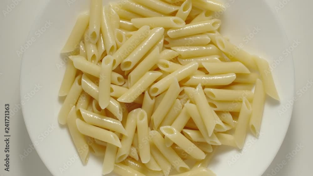 SLOW MOTION: Penne pasta falling into a white plate - Top View SLOW MOTION: Penne pasta falling into a white plate - Top View