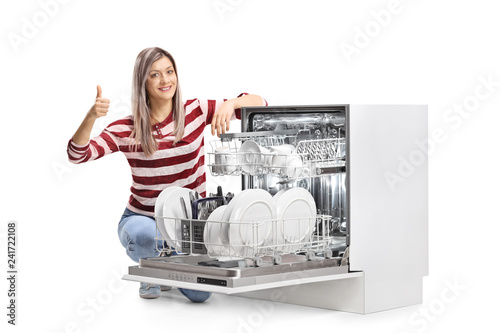 Young smiling woman with an open full dishwasher giving thumbs up