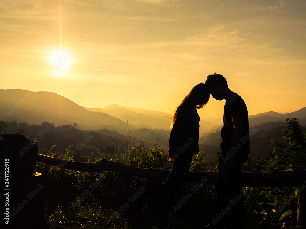 Silhouette of happy young couple in love looking view sunset on the mountain. Romantic couple in love kissing.