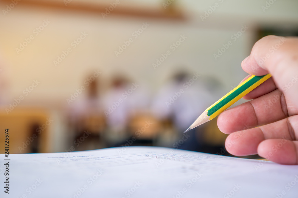 Students hands taking exams, writing examination room with holding pencil on optical form of standardized test with answers and english paper sheet on row desk chair doing final exam in classroom. Students hands taking exams, writing examination room with holding pencil on optical form of standardized test with answers and english paper sheet on row desk chair doing final exam in classroom.