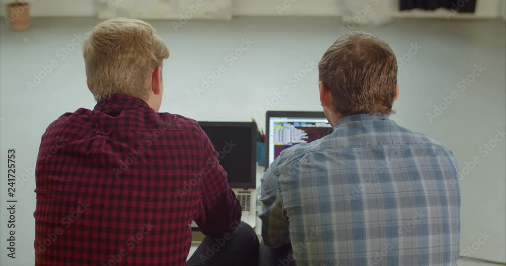 Rear view of two outsource software developer looking at computer screen and discussing source codes while working on project at creative office. IT programmers with laptops typing lines of HTML code. Rear view of two outsource software developer looking at computer screen and discussing source codes while working on project at creative office. IT programmers with laptops typing lines of HTML code.