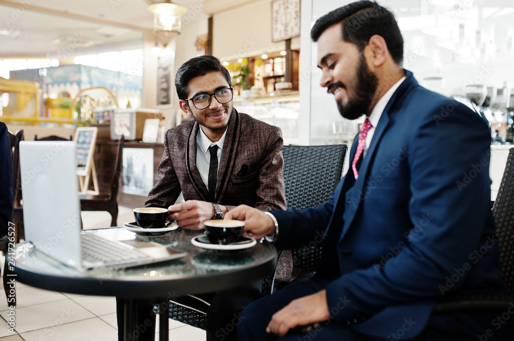 Two indian business man in suits sitting at office on cafe, looking at laptop and drinking coffee.