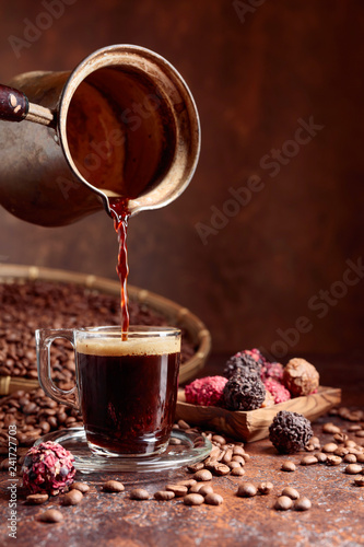 Black coffee is poured into a small glass cup from a copper coffee maker.