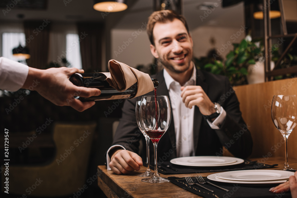 selective focus of attractive man in suit smiling and sitting in restaurant selective focus of attractive man in suit smiling and sitting in restaurant
