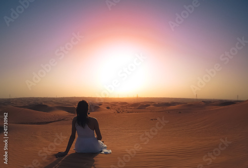 a girl in a dress sits on a hill in the desert and admires the sunset. the view from the back © _KUBE_