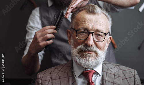 Portrait of concentrated grey haired businessman having his hair trimmed in a barber shop. Concept of grooming photo