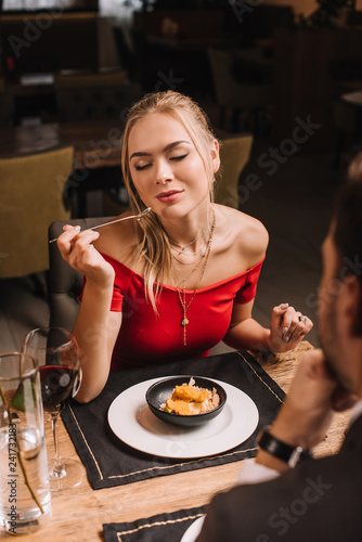 girlfriend eating sweet dessert while sitting near boyfriend in restaurant