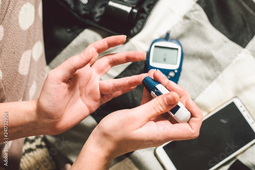 Theme diabetes. A close-up macro plan. Hands of a young Caucasian woman at home in the bedroom on the bed. It uses the technology of an instrument for measuring the level of glucose in the blood