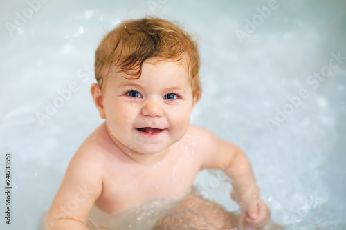 Adorable cute little toddler girl taking bath in bathtub. Happy healthy baby child playing with rubber gum toys and having fun. Washing, cleaning, hygiene for children