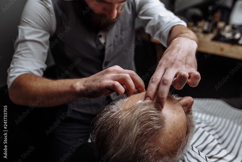 Close up shot of professional man s hair stylist shaving old man in a modern barbershop. Close up shot of professional man s hair stylist shaving old man in a modern barbershop.