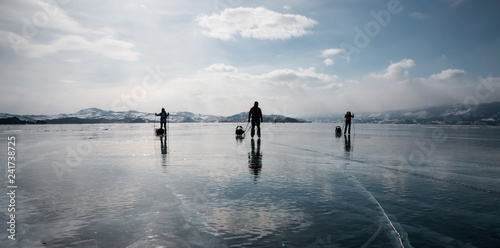 Three travellers on skates on the ice of Baikal lake, Siberia
