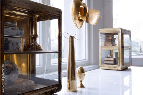 Dekoration in Gold und Messing auf weissem Tisch vor Fenster in heller Altbauwohnung photo