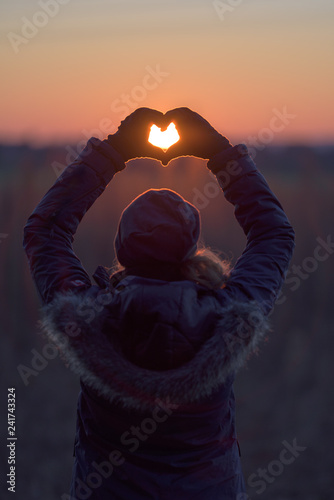 Two hands forming heart shape front of sun